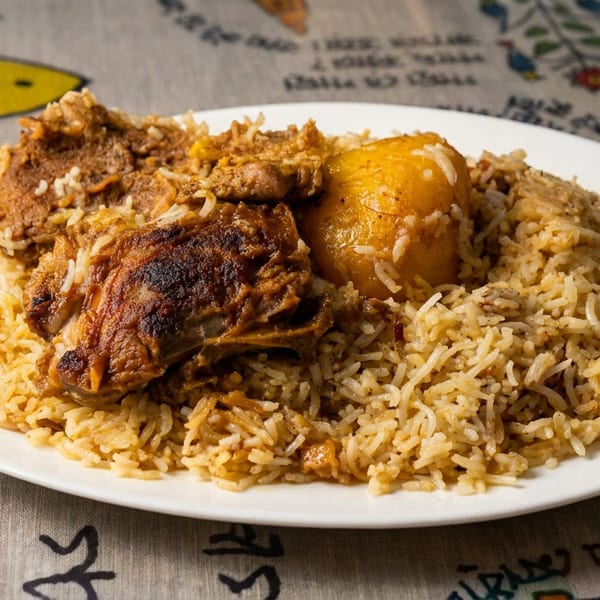 Plate of spiced rice topped with roasted meat and a golden boiled egg on a colorful illustrated tablecloth.