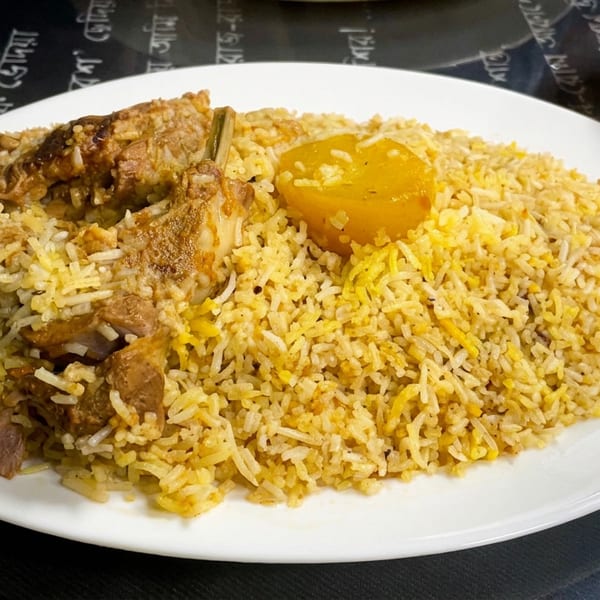 Plate of spiced rice with tender meat and a boiled egg, served beside a bowl of fresh salad.